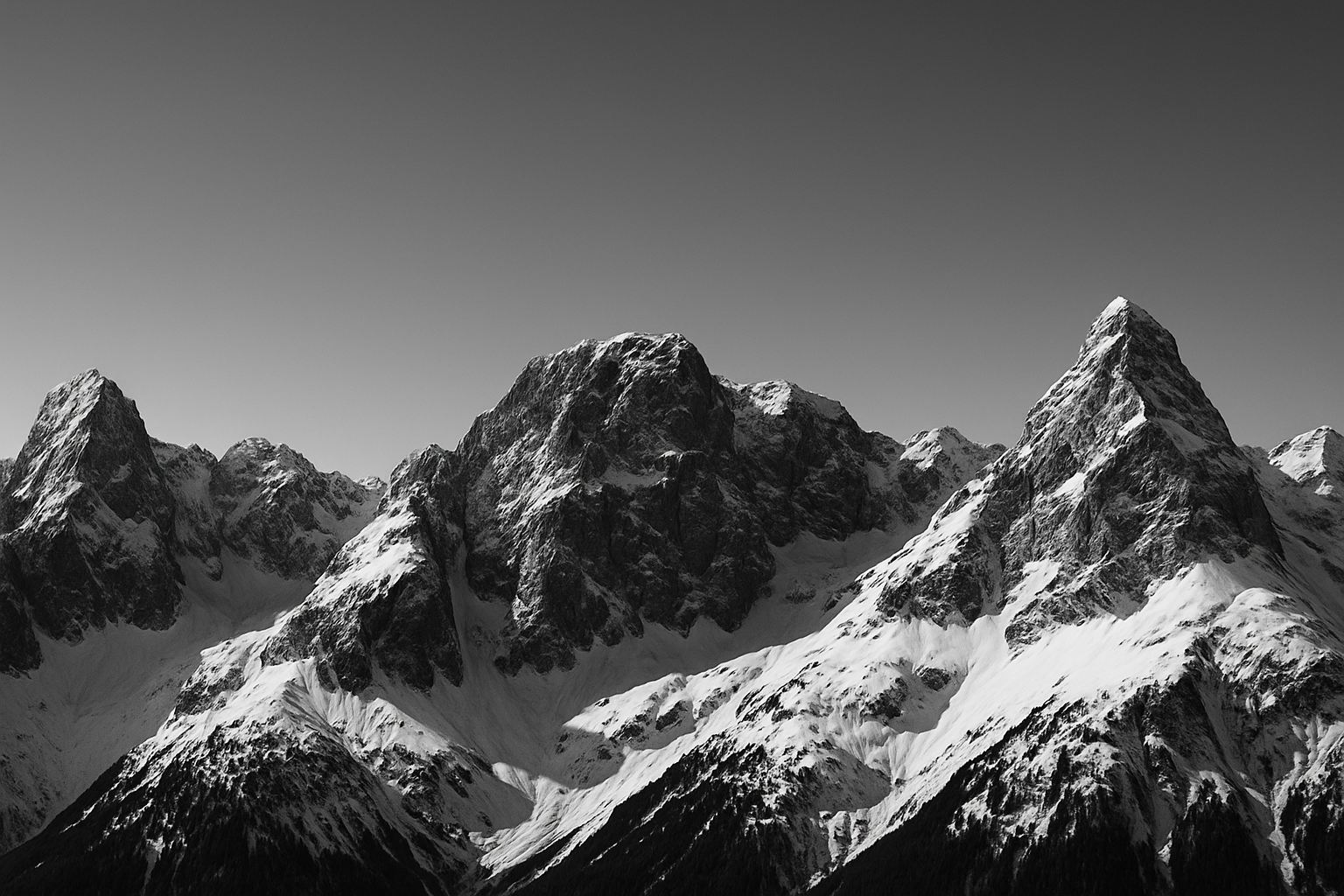 A wide panoramic view of majestic snow-covered mountains under a clear sky, captured in black-and-white. The peaks are rugged, dramatic, and towering, with deep shadows and sharp contrast that highlight the texture of the rocky cliffs and snowy slopes. A minimal, cinematic atmosphere perfect for a website banner background. Aspect ratio 16:9, ultra high-resolution, clean composition with empty space for text overlay